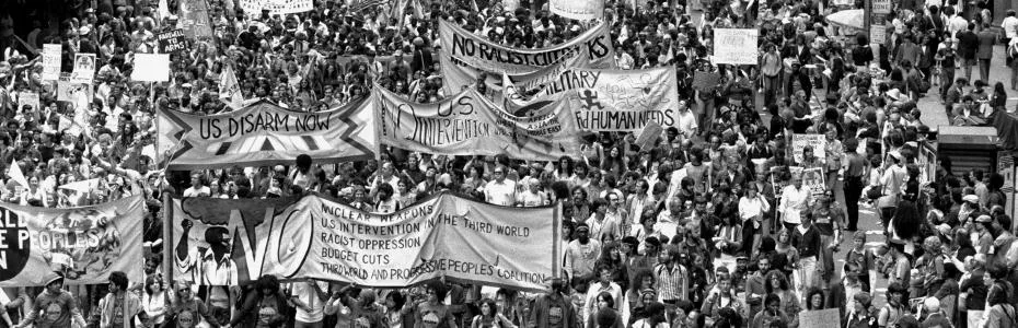 Marchers fill a city street behind hand-painted banners reading US Disarm Now, during a 1980s nuclear disarmament demonstration.