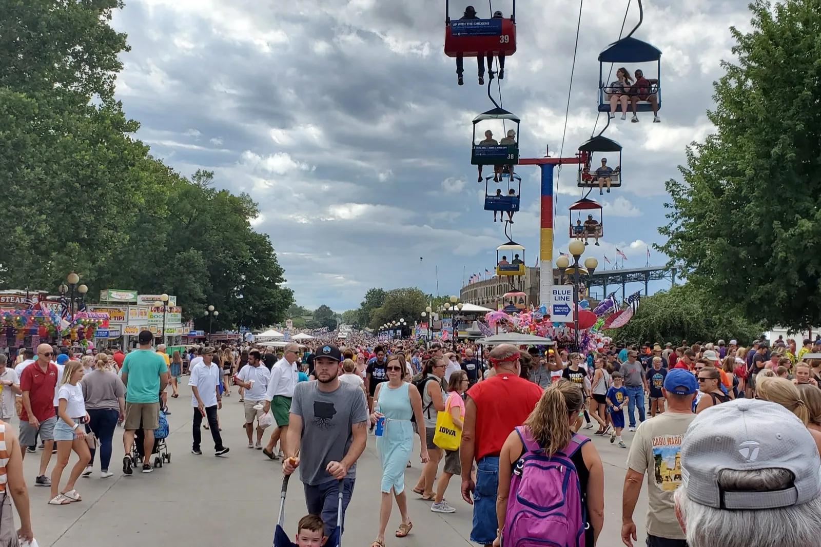 A packed crowd walks the Grand Concourse at the Iowa State Fair, with the Sky Glider ride overhead.